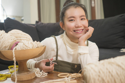 亚洲女孩享受流苏手工爱好-年轻快乐和漂亮的韩国妇女在家里做macramé使用绳子，绳和线在国内手工装