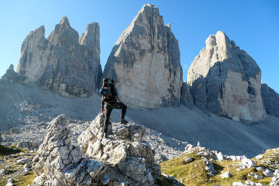 一名男子站在一块巨石上，欣赏意大利Dolomites地区的Drei Zinnen山的近景。尖锐而高大