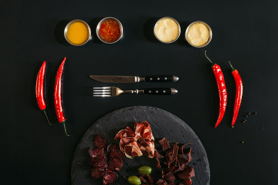 石板板上的美味什锦肉，刀叉，各种酱汁和辣椒