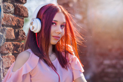 美丽的红发女士听音乐耳机在模糊的背景和红墙砖在日落