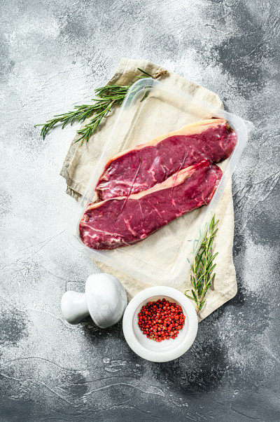 鲜肉，真空包装大理石牛肉，腰肉排。黑暗的背景。空间的文本。超市包装