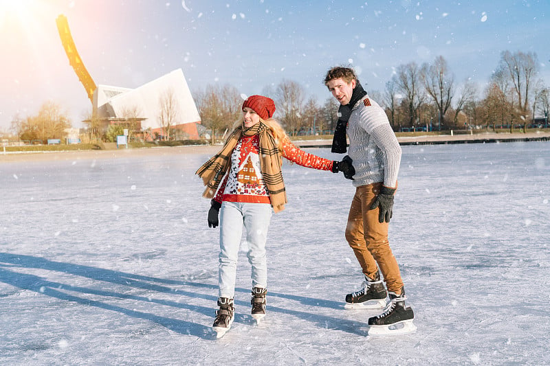 穿着温暖毛衣的情侣在冰上玩耍。女人和男人在阳光明媚的下雪天在户外滑冰。冬季平安夜在冰上竞技场上的活跃