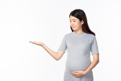 年轻美丽的孕妇站着，触摸腹部显示空白的副本空间在开放的手掌上的文字在白色的背景。怀孕、母性、人与期望