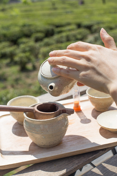 以绿茶田为背景手工倒绿茶。