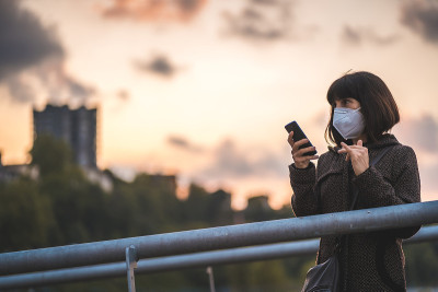 一个戴着面具的黑发姑娘在夕阳下发送音频信息。首次接触未受控制的Covid-19大流行