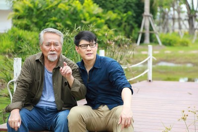 一个快乐的亚洲老人坐在河边的码头上，把他的生活经验传授给他的儿子