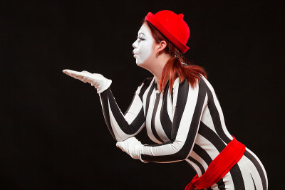 女哑剧艺术家的肖像表演，孤立在黑色的背景。女人飞吻在条纹裙子摆姿势