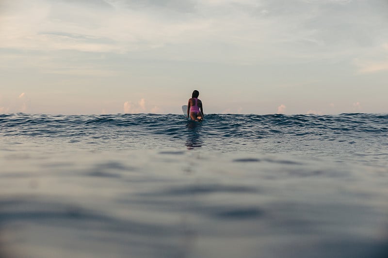 在日落时在海上冲浪板上的冲浪者的后视图