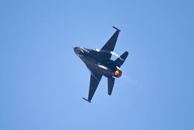 近距离观察一架F-16猎鹰战斗机在大G转时，机翼根部有凝结条纹，加力燃烧器打开