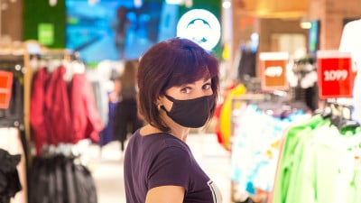 在疫情期间，一名戴着黑色防护口罩的妇女在购物中心与拿着东西的人在一起
