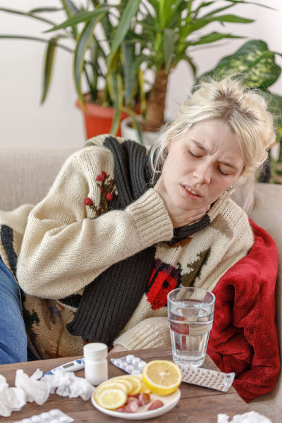 穿毛衣的女孩躺在沙发上生病了。感冒和流感。病人感冒了，觉得不舒服而且喉咙痛。不健康的女孩喉咙痛