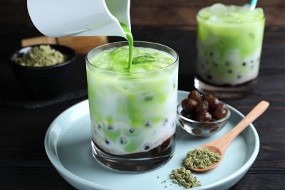 在黑色的木桌上，倒入绿色抹茶和奶茶，特写