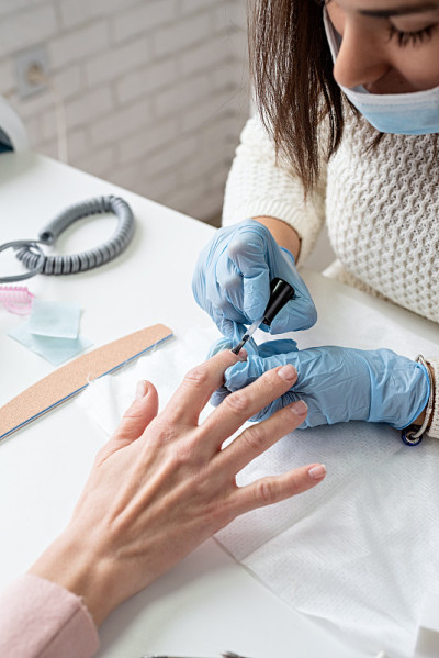 Manicure master in mask and gloves putting on gel 