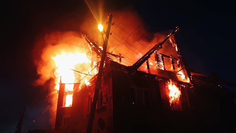 房子的屋顶着火了。居民楼烧了，村。消防队员从上面的起重机上灭火。烟雾和火花。