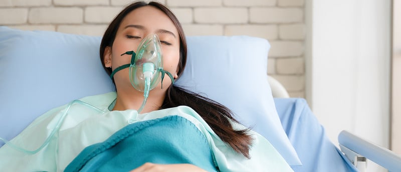 亚洲妇女病人在医院的床上戴着氧气面罩
