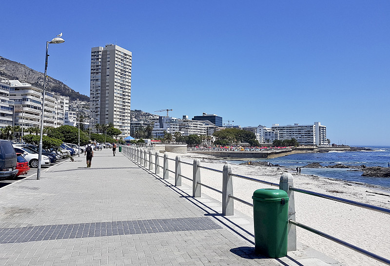 山脉，酒店和深蓝色的海水和海浪在海点，海滩漫步在南非开普敦。