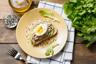 木桌背景上放着鳄梨、金枪鱼罐头和煮鸡蛋吐司。健康食品，早餐或午餐吃鳄梨三明治。