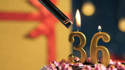 生日蛋糕号36支金色蜡烛用打火机点燃，背景礼物用黄色礼盒用红丝带系好。特写镜头