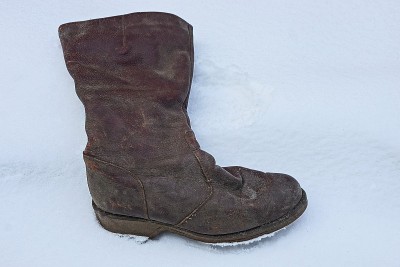 一只又旧又脏的棕色皮靴放在一堆白雪中