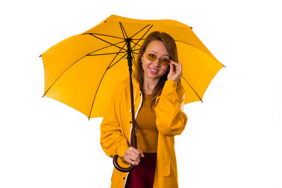 微笑的女孩穿着黄色雨衣站在伞下，孤立在白色的背景上