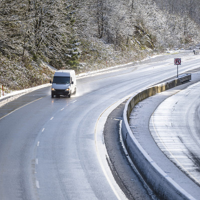 白色小型商业货车在潮湿的雪地上行驶，路上有树