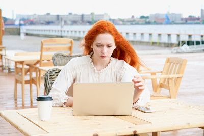 Redhead female looking at laptop in cafe outside