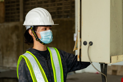 年轻的亚洲女工程师戴着医用口罩遮住嘴，戴着白色安全帽