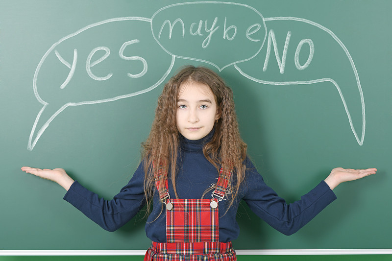 女学生在绿色学校董事会附近。微笑的小女生在绿色校董会旁繁殖手臂。