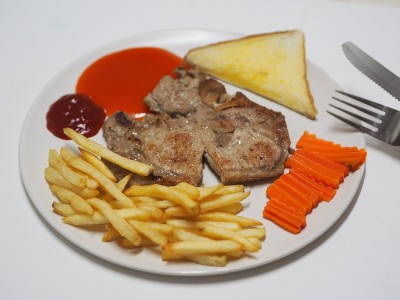 带骨牛排猪肉配蔬菜沙拉，吐司和炸薯条，放在白盘子里烹调食用