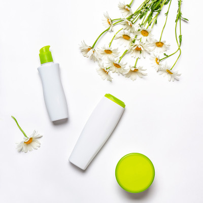 护理化妆品在时尚的瓶子与洋甘菊雏菊花在白色的背景。水疗、美容、美容概念。平铺，俯视图，复制空间，模拟
