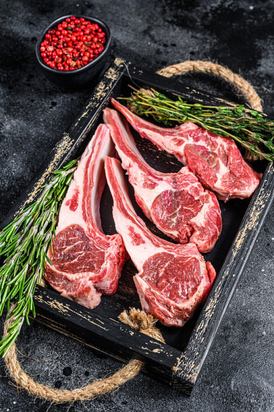 生羊肉放在木托盘里。黑色背景。俯视图