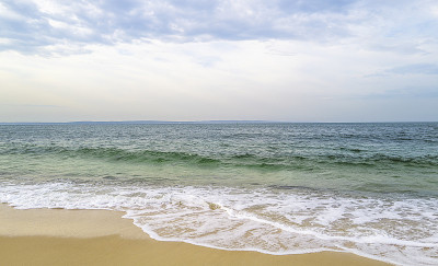 热带蓝绿色的海水和海滩上的白色波浪。背景是柔和的蓝天上的白云。