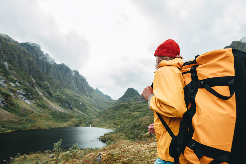 游客背包站在前面的山脉，而旅途由斯堪的那维亚。男性旅行者穿着黄色夹克探索国家公园和徒步旅行的户外景观