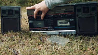 草地上有一台老式录音机。人调整设备上的声音