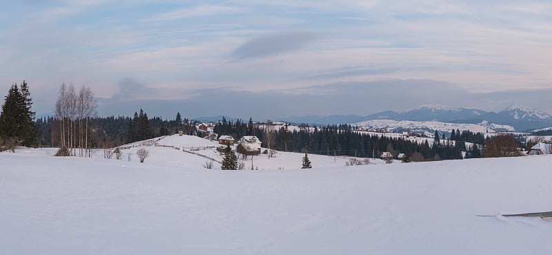 小高山村庄和冬季雪山在第一轮日出阳光的周围，沃罗年科，喀尔巴阡，乌克兰。