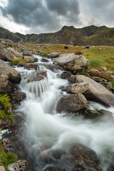 秋天，在斯诺登尼亚的Llyn Ogwen和Llyn Idwal附近，一条河流顺着山脉流下的穆迪景观图