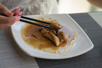 一位女士正在吃一道用鸡肉和照烧酱做的亚洲菜