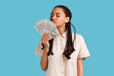 留着黑头辫的女人手里捧着一把大扇子，愉悦地嗅着美元钞票。