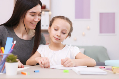 妈妈帮助女孩做家庭作业。孩子和父母。