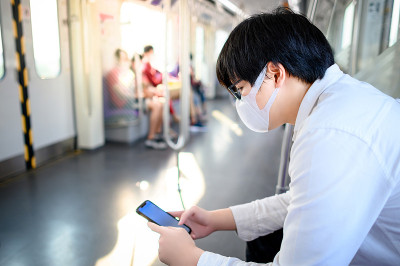 亚洲男子戴着面具在空中列车上使用手机