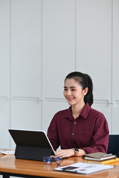 微笑的女商人坐在她的办公桌和工作与电脑平板电脑。