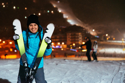 傍晚时分，一个女人站在白雪覆盖的山顶上滑雪