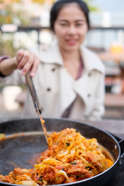 模糊的女人背景微笑，并展示如何烹饪韩国食物称为“Dakgalbi”辣烤鸡，她参观韩国餐厅著名的菜单，