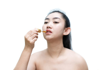 在白色背景下，手持舌下滴管大麻油的女子