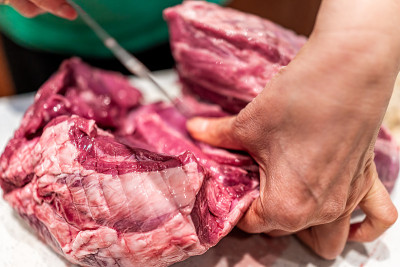 红色生牛肉或羊肉全腿大块与女人用刀切块在砧板上烹调准备