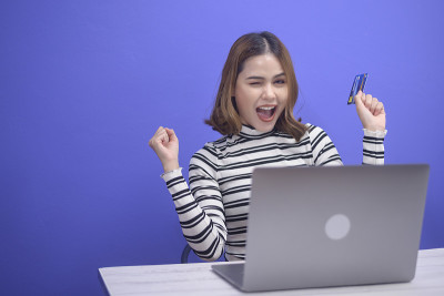 一个快乐的年轻女子拿着信用卡，用手提电脑在网上购物