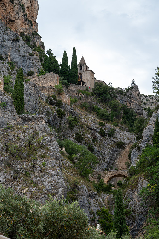 在法国普罗旺斯偏远的中世纪村庄Moustiers-Sainte-Marie，欣赏山崖、老房子、绿色山