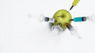 杀虫剂、硝酸盐、转基因和其他化学物质被用注射器注射到青苹果中。前视图。