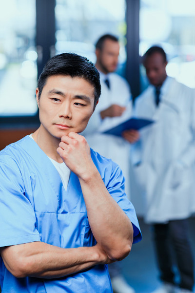 肖像沉思医生在医疗制服与同事在后面的诊所