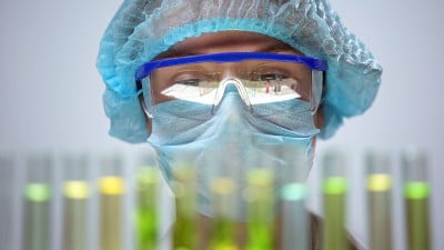 女研究人员在防护口罩中分析试管反应，实验